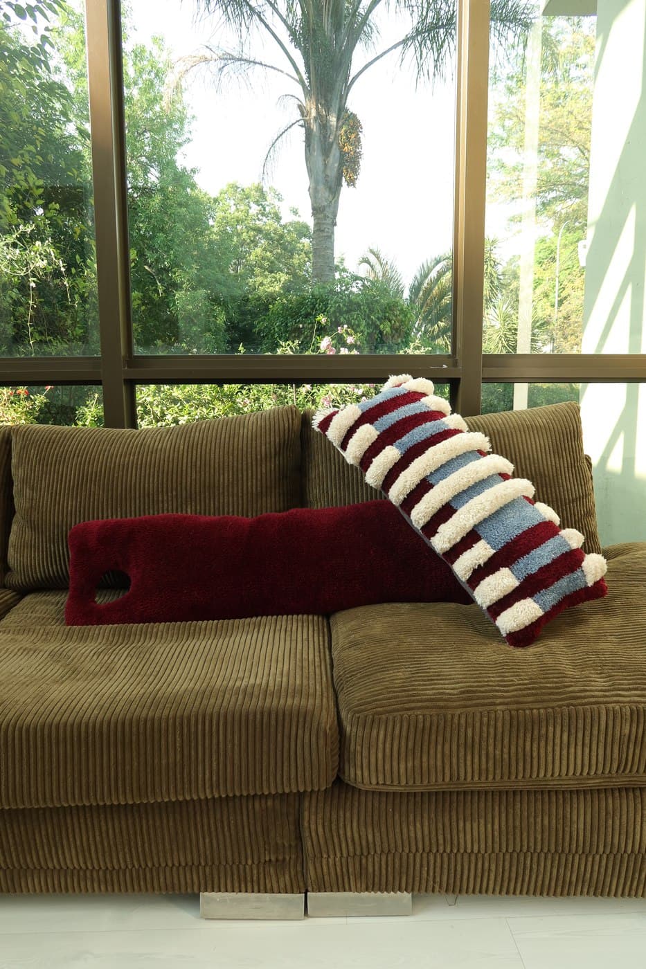 A long bolster cushion and a red, blue, and cream striped scatter cushion on a sofa