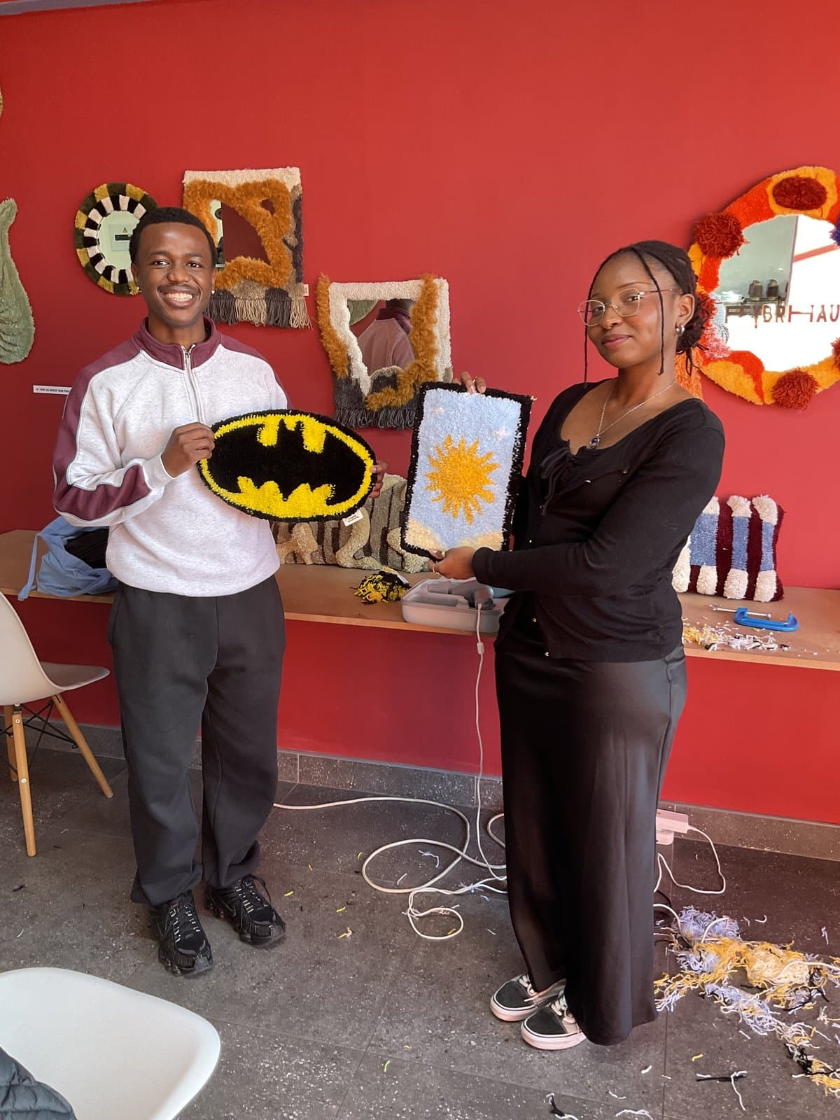 Two students holding a Batman-logo rug and a flower rug