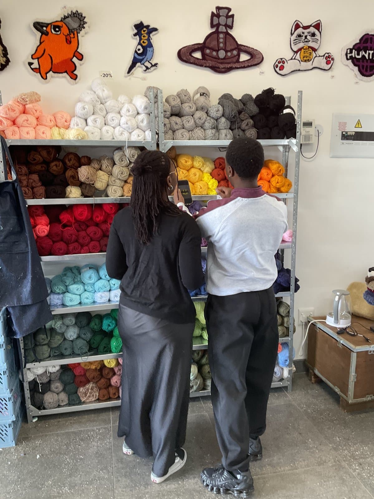 Students chatting in front of the studio's yarn shelves
