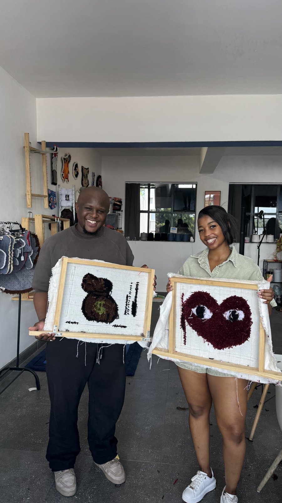 Two students holding up their finished tufted rug pieces