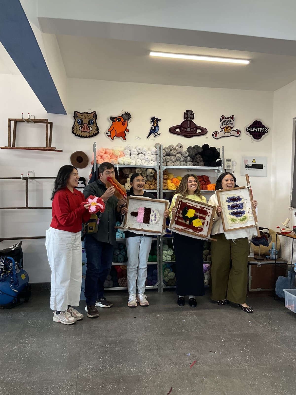 Students holding their tufted pieces in front of the yarn wall