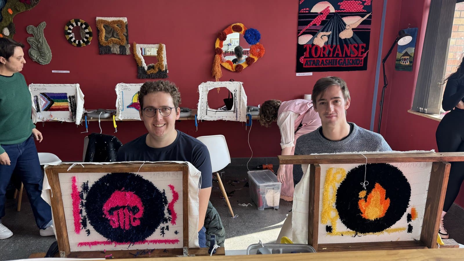 Two people holding up circular tufted rugs with sun designs