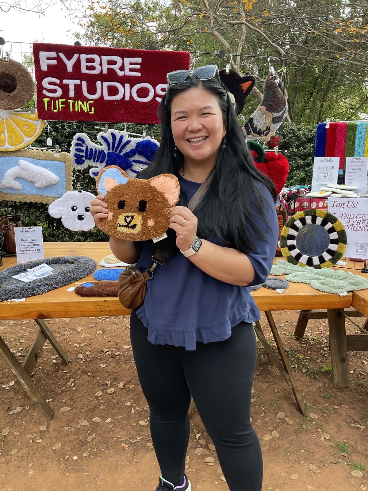 Woman holding a tufted teddy bear patch at a market stall